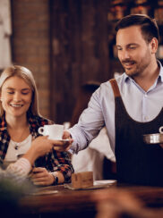 smiling-waiter-serving-coffee-female-guests-cafe